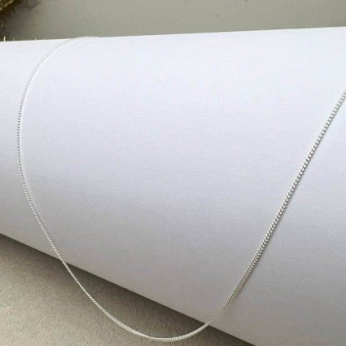 Sterling silver delicate curb chain in 925 material, presented on a curved white surface.