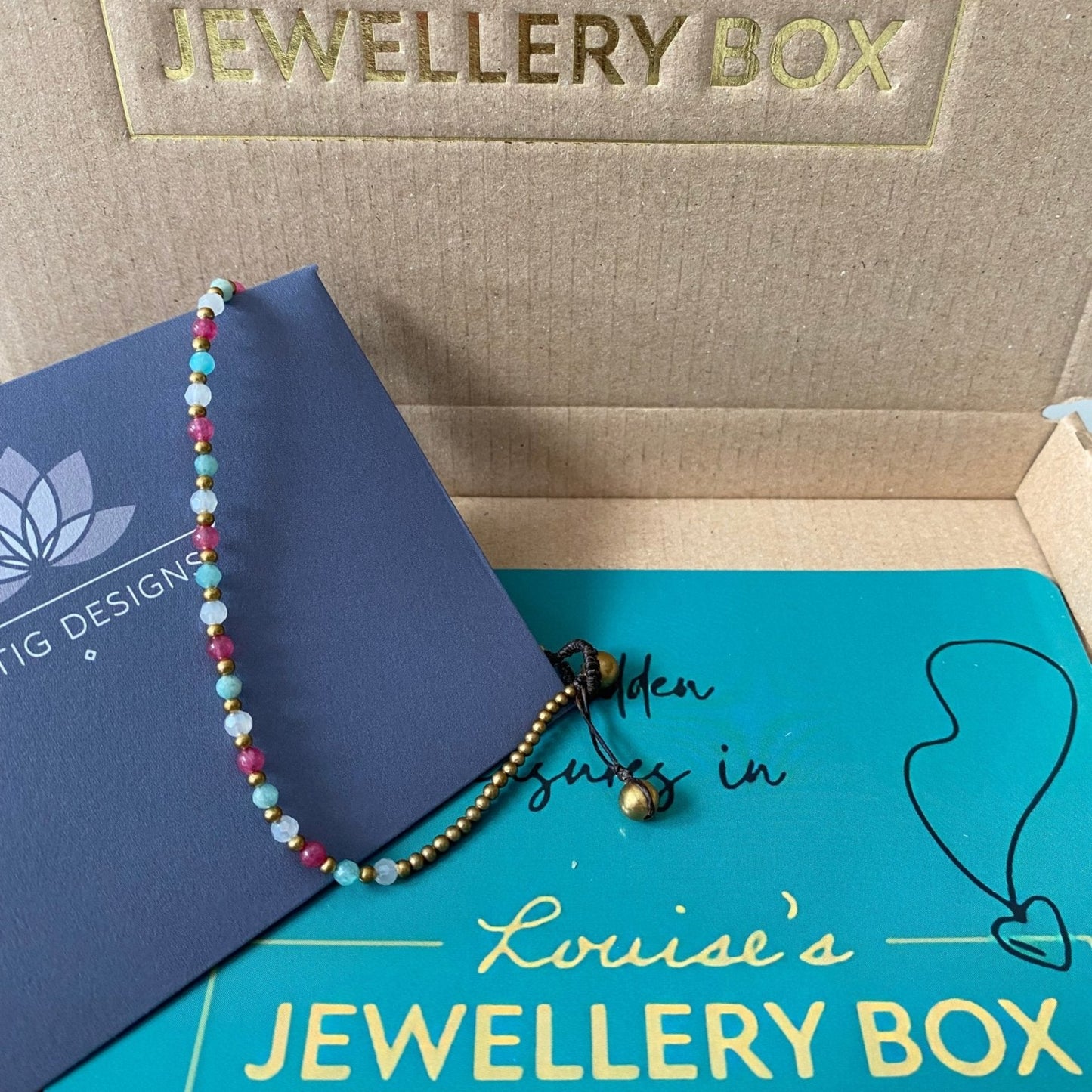 Amazonite crystal healing anklet for health with gold beads on a knotted cord, displayed on branded packaging.