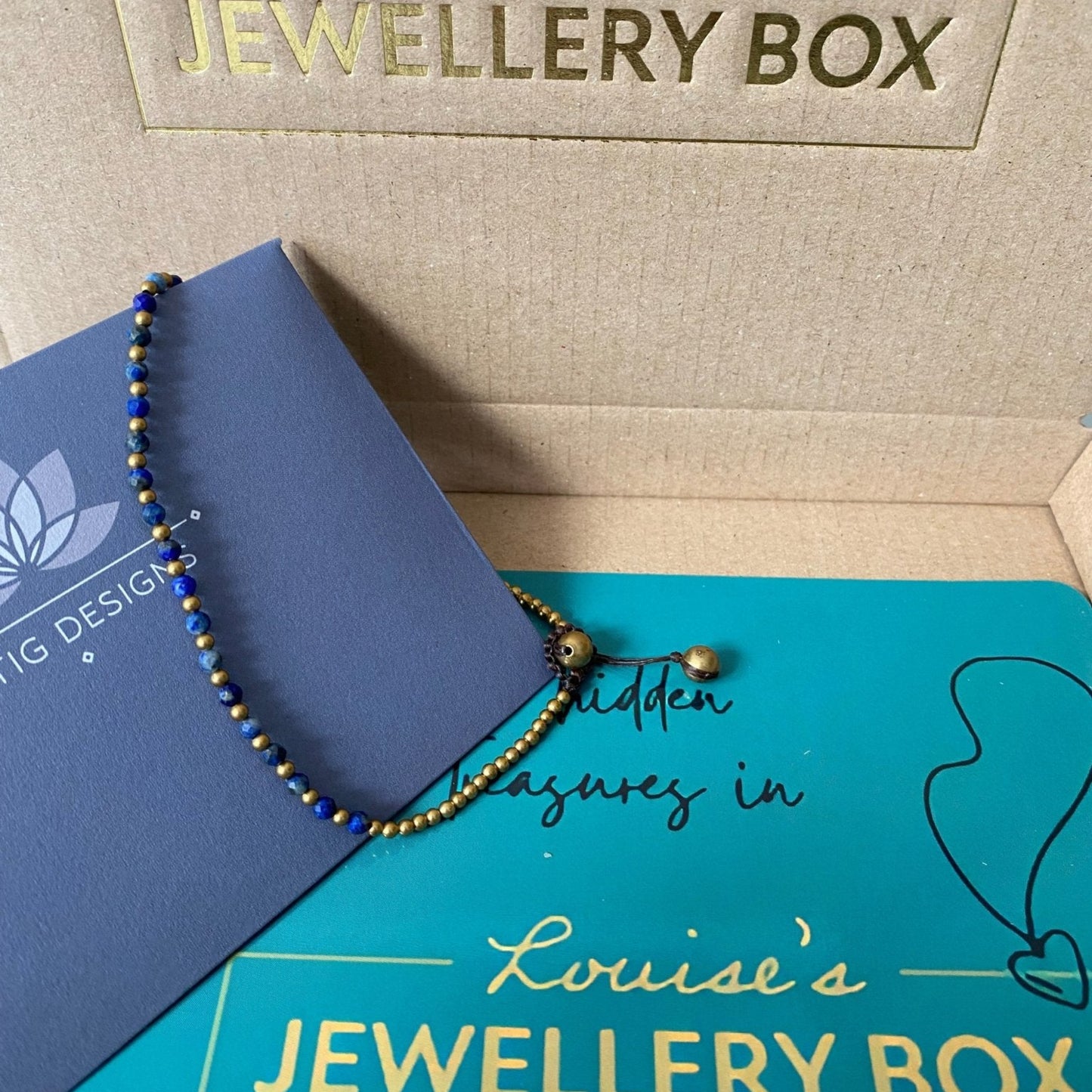 Blue and gold beaded Lapis anklet for insecurity, displayed on a blue card and turquoise box.