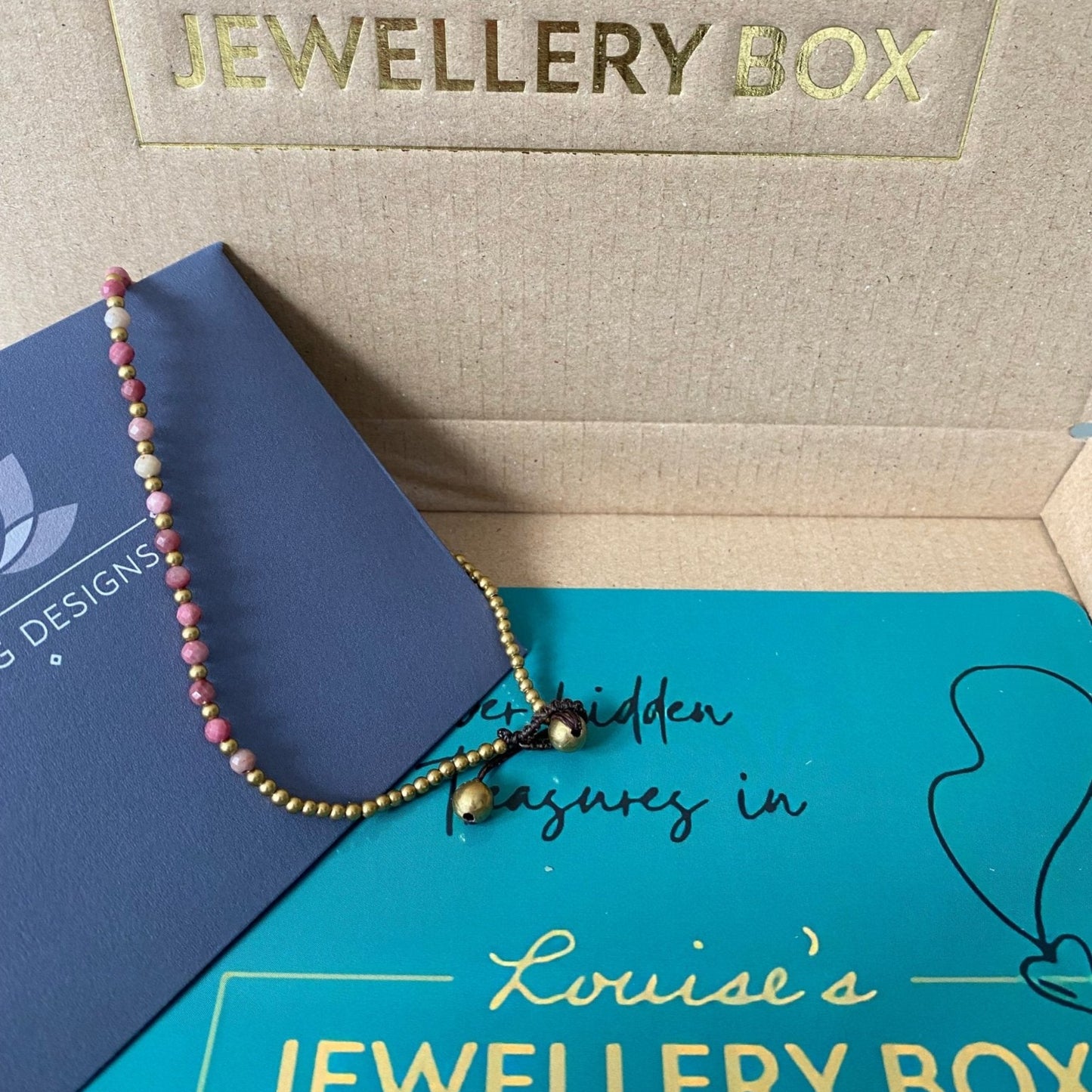 Pink tourmaline crystal healing anklet for friendships with gold accents, lying on a presentation box.