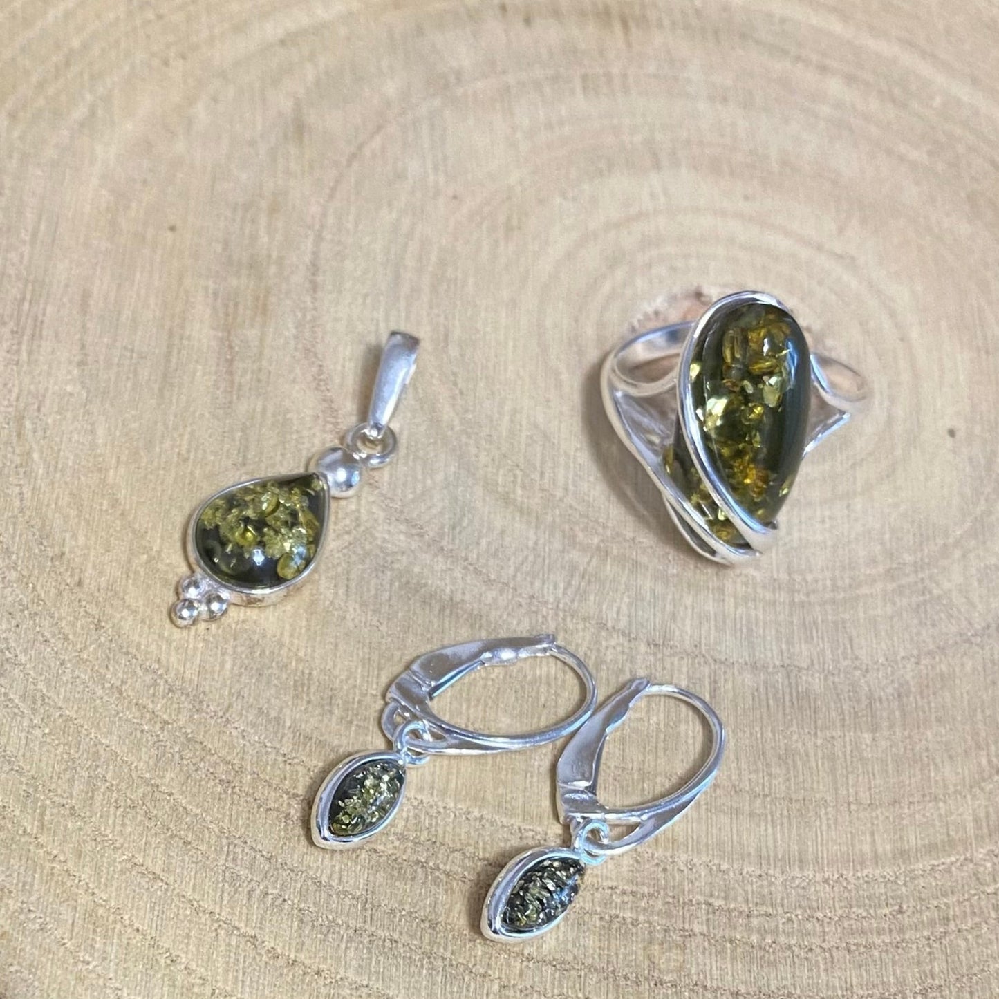 Green Baltic amber teardrop pendant in sterling silver showing natural inclusions with matching earrings and ring
