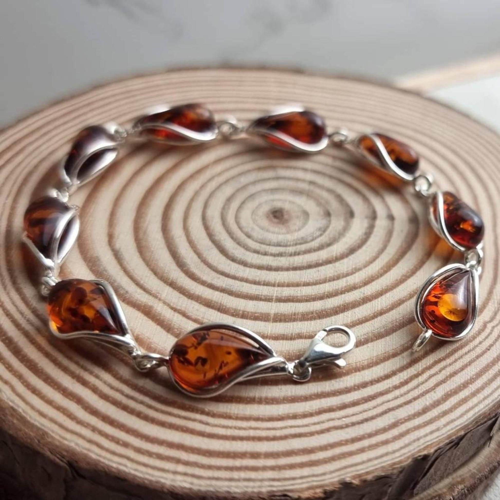 Modern bracelet in sterling silver with cognac Baltic amber, set on a wooden ringed surface.
